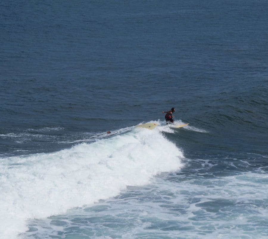 Surfeur attendant la vague au coucher du soleil sur la côte sud de Bali, silhouette sur fond d’océan et d’ambiance balinaise authentique.